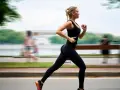 Donna bionda in abbigliamento sportivo nero corre con una postura corsa perfetta lungo un percorso alberato.