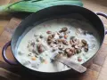 Un plat de blanquette de veau facile mijote dans une cocotte, garni de champignons et de carottes. Un poireau est posé à côté.