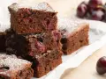 Saftige Stücke von Omas Schoko-Kirsch-Kuchen, bestäubt mit Puderzucker. Kirschen sind im dunklen Teig sichtbar.