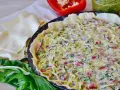 Tarte salée garnie de fromage, poivrons et ail des ours, prête à cuire. Pâte feuilletée et poivron rouge à côté.