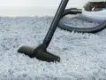 Vacuum cleaner head on a fluffy grey rug, demonstrating how to wash a rug by removing dust and debris.