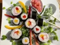 Kolorowe rolki sushi z surimi, papryką i mango, ozdobione szczypiorkiem i papryczkami chili. Obok wasabi i marynowany imbir.