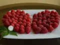 Dwie kupki malin, jakby serce, z monetą i listkiem. To malina husaria, pyszna i cenna.