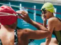Deux nageuses se préparent pour une course de nage brasse. L'une ajuste ses lunettes, l'autre sourit.