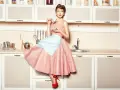 Kobieta w stylu moda lat 50. w kratkę, z fartuszkiem i filiżanką kawy w kuchni.