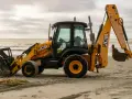 Żółta koparko-ładowarka firmy JCB stoi na piaszczystej plaży, gotowa do pracy.