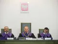 Trzech sędziów w togach podczas jawnego posiedzenia sądu. Na ścianie wisi godło Polski.