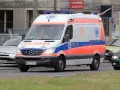 Karetka na sygnale z oznaczeniami medycznymi, jadąca ulicą.