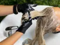 Fryzjerka w czarnych rękawiczkach nakłada odżywkę na blond włosy. Zastanawiasz się, czy farba do włosów się zmywa?