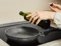 Ręka wylewa oliwę z oliwek do smażenia na patelnię.