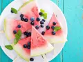 Erfrischendes Wassermelonen Eis mit Blaubeeren und Minze auf Eiswürfeln, serviert auf einem weißen Teller.