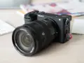 Appareil photo Sony Alpha a6700 prêt pour un test. Un objectif noir est monté, avec un clavier blanc et des documents flous en arrière-plan.