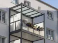 Nowoczesny balkon dostawny z przeszklonym zadaszeniem i balustradą, ozdobiony skrzynkami z kwiatami. Sprawdź balkon dostawny cena.