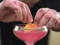 Ręce dekorują drinka skórką pomarańczy. To ostatni krok w przygotowaniu Cosmopolitan przepis.