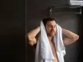 Uomo si asciuga i capelli con un asciugamano bianco. Peccato che non arriva acqua calda solo nella doccia, altrimenti sarebbe stato un bagno perfetto.