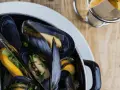En stor kastrull med ångande blåmusslor, perfekt för en måltid med vin till moules frites. Pommes frites syns i bakgrunden.