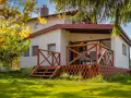 Bungalow z drewnianym tarasem i schodkami, otoczony zielonym ogrodem i kwitnącym drzewem.