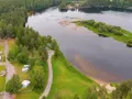Vacker vy över Selholmens camping med husbilar och stugor vid en sjö omgiven av skog.