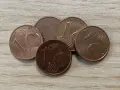 Cinq pièces de 1 centime d'euro, certaines semblant être une pièce de 1 euro rare valeur, sont disposées sur une surface en bois.