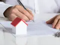 Mann unterschreibt Mietvertrag in Wuppertal. Ein kleines Hausmodell und Schlüssel liegen daneben.