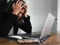 Kobieta z rękami na głowie przy laptopie, wyrażająca frustrację i myśląc o porzuceniu pracy.