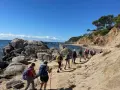 Une randonnée côtière ensoleillée, avec un groupe de randonneurs profitant d'une marche afghane le long d'une plage rocheuse et d'une falaise verdoyante.