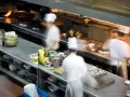 Chefs en movimiento en una cocina profesional, con ollas humeantes y ingredientes listos. El "mise en place" es clave para la eficiencia.