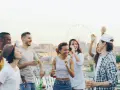 Un groupe d'amis souriants et dansant sur un toit, avec une grande roue en arrière-plan.