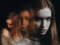 Rozmyta twarz młodej kobiety, jakby w transie. W tle kolejne, niewyraźne postacie. Czy to jej wewnętrzny świat, czy może chad?