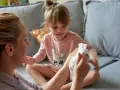 Mama pokazuje córce pieluchę, symbolizując etap, kiedy dziecko przestaje nosić pieluchy.