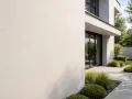 Un mur extérieur en enduit taloché blanc, avec une texture subtile, bordant un jardin moderne aux lignes épurées.
