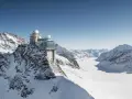 A modern building with glass walls and domes sits atop a snowy mountain, offering breathtaking views of the surrounding peaks and a vast glacier. This is the top of Europe, a place of incredible altitude.