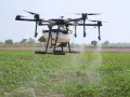A drone sprayer, one of the types of drones in agriculture, hovers over a field, dispensing liquid onto crops.