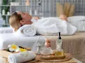 Relaks w jednym z hoteli spa Polska. Kobieta w białym szlafroku leży na łóżku, otoczona kosmetykami i kwiatami.