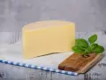 Kawałek żółtego sera na desce, obok gałązka bazylii. Uważaj na uczulenie na ser żółty objawy, jeśli wystąpią.