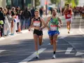 Atleti si preparano a una maratona, correndo fianco a fianco. La folla incita lungo il percorso.