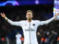 Neymar w białej koszulce PSG, z charakterystyczną neymar fryzurą, unosi ręce w geście radości na tle rozmazanych świateł stadionu.