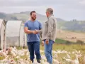 Dwóch rolników wita się na farmie z kurami, symbolizującym sukces w hodowli i troskę o klasy ziemi.