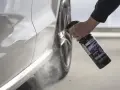 En hand sprutar Sonax kallavfettning på en vit bil.