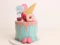Bunter Drip Cake mit rosa Glasur, Lollis, Macarons und einem Eiswaffel-Horn.