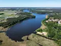 Malownicze jezioro Wojnowskie otoczone lasami i polami. W oddali widać zabudowania wsi, a na brzegu plażę z pomostem.
