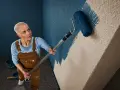 Frau mit Kurzhaarschnitt streicht mit blauem Roller eine Wand mit Rauputz.