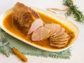 Redondo de ternera jugoso en salsa, cortado en rodajas, servido en plato ovalado blanco.