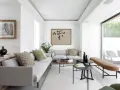 Salón moderno con sofás grises, mesas bajas negras y marrones, y un banco de cuero. Grandes ventanales conectan el interior con la terraza, creando un espacio fluido para unir terraza y salón.