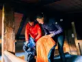 Préparation pour une nuit en refuge. Un homme en veste rouge et une femme en veste violette déballent des sacs de couchage dans une cabane en bois.