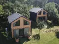 Dwa nowoczesne domki z drewna i czarnego panelu, idealne projekty domów pod wynajem, otoczone zielenią.