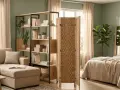 Un dormitorio integrado en el salón, con un sofá, estanterías y una cama separada por un biombo de fibras naturales.