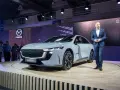 Elegancki, szary sedan Mazda6e prezentowany na scenie przez mężczyznę w garniturze.