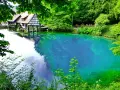 Der Blautopf See lädt zum Schwimmen ein. Ein historisches Fachwerkhaus mit Wasserrad spiegelt sich im kristallklaren, blauen Wasser.