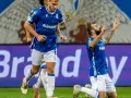 Piłkarz klęczy na boisku, celebrując bramkę. W tle biegnie kolega z drużyny. Wszyscy w niebieskich strojach. Czekamy, kiedy wraca ekstraklasa!